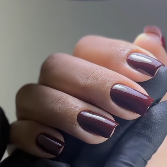 Esmaltação em gel em tom vinho, com brilho espelhado e contorno encaixado junto à cutícula