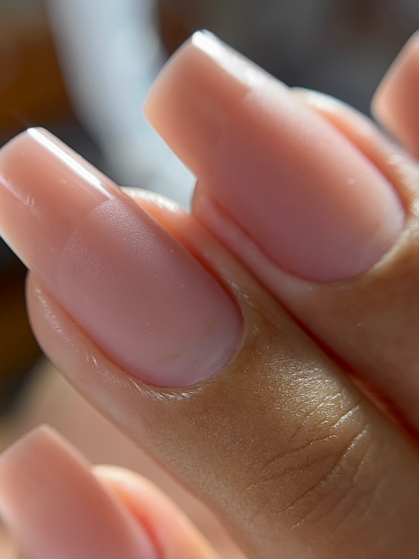 Close vertical de unhas em tom nude, com superfície nivelada e contorno encaixado junto à cutícula