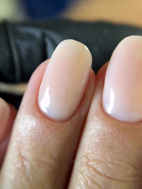 Unhas em gel leitoso com formato oval, brilho espelhado e contorno limpo junto à cutícula