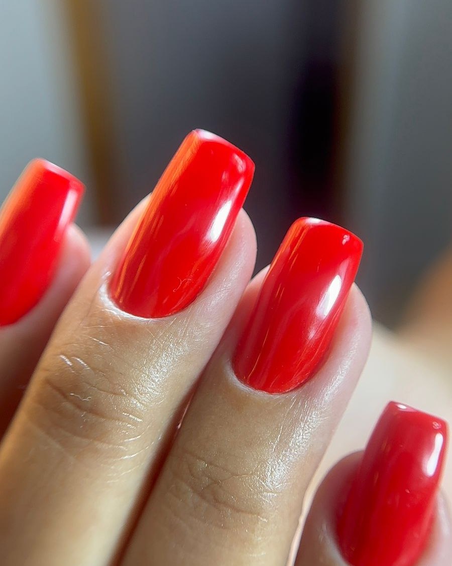 Unhas com esmaltação em gel vermelha, brilho espelhado e contorno limpo junto à cutícula